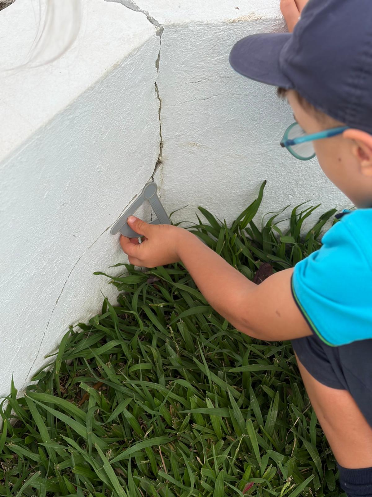 Criança de óculos e boné a encostar o esquadro ao canto de um muro branco